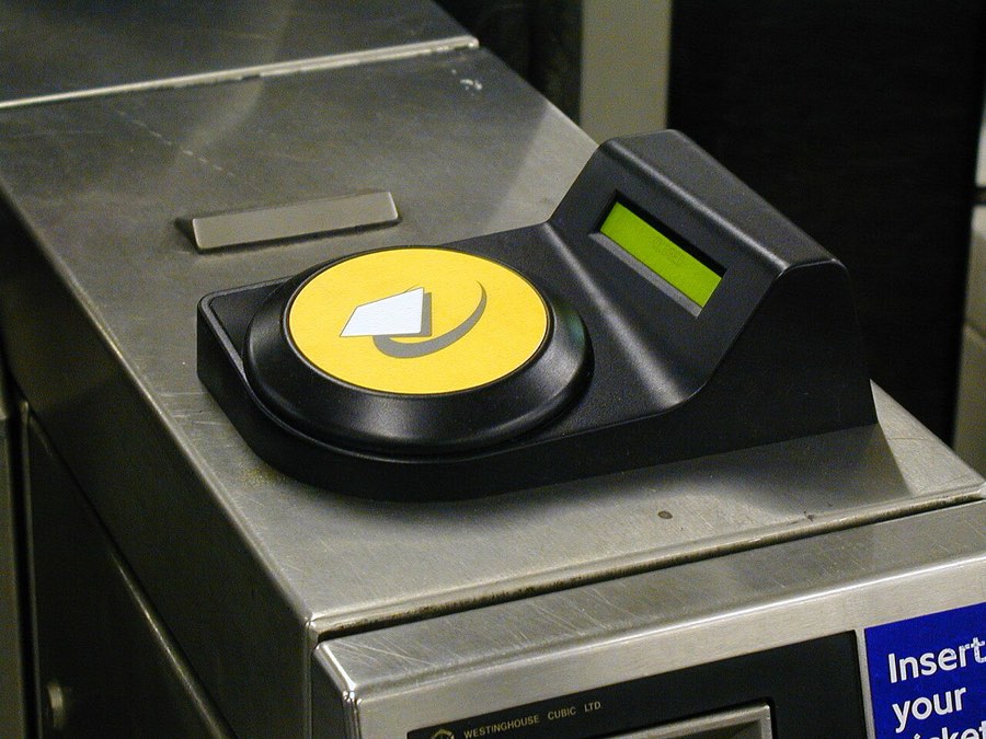 A round yellow contactless pad on top of a London Underground ticket gate, with a green indicator light beside it